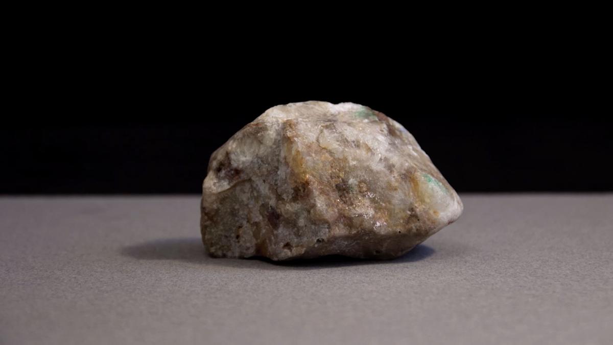 A close up of a brain shaped rock. The rock is cream coloured with green and yellow details, it has a crystal like texture.